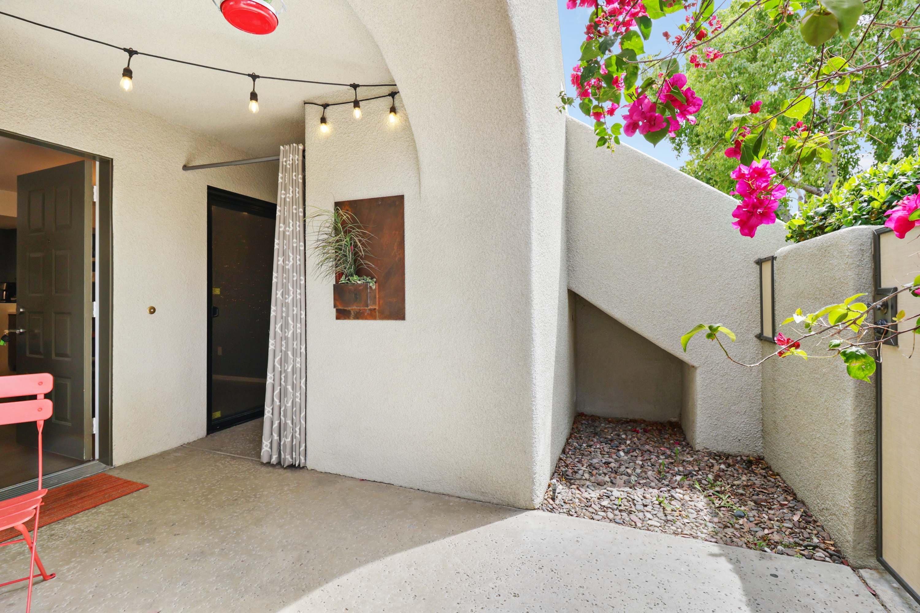 An outdoor area with a concrete floor, a red bench, a door, a curtain, a potted plant, and a wall with a textured finish.