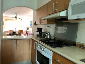 A kitchen with wooden cabinets, a stove, a microwave, and a dining area with chairs and a table. - APARTMENT IN ACAPULCO DIAMANTE IN FRONT OF GNP ARENA (Acapulco de Juárez)