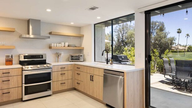 A modern kitchen with built-in appliances, wooden cabinets, and a large sliding glass door leading to an outdoor patio. - Resort Style Condo Getaway in Monterey Country Club (Palm Desert)