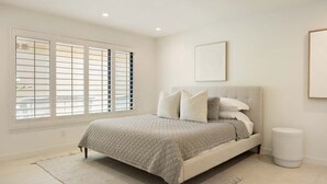 A bedroom with a bed, a window with blinds, a bedside table, and a wall-mounted artwork. - Resort Style Condo Getaway in Monterey Country Club (Palm Desert)