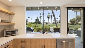 A modern kitchen with a large window, wooden cabinets, a dishwasher, and a built-in toaster. - Resort Style Condo Getaway in Monterey Country Club (Palm Desert)