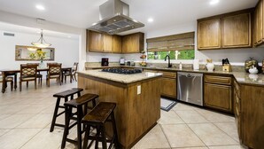 Een moderne keuken met houten kastjes, een centraal eiland, barkrukken, een vaatwasser en een raam met uitzicht.