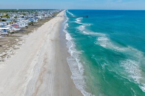 Une plage côtière avec une jetée qui s’avance dans l’océan, bordée d’une rangée de maisons.