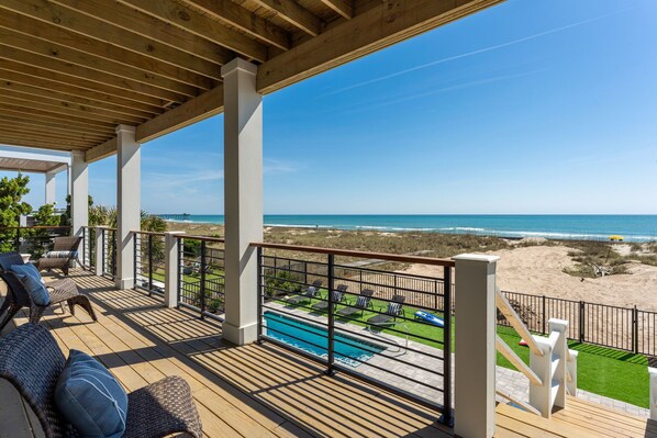 A wooden deck with outdoor seating, a pool, and a view of the beach.