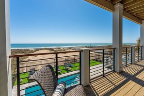 A balcony with a view of the ocean, a pool, and outdoor seating.