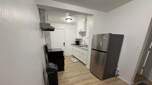 A narrow kitchen with a stainless steel refrigerator, a black trash bin, and a wooden floor. - 1BR Sleep 4 S Amarillo Corp Stays Tech + Hospital (Amarillo)
