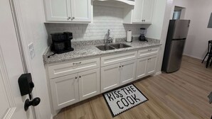 A kitchen with white cabinets, a granite countertop, a stainless steel refrigerator, and a 'KISS THE COOK' doormat. - 1BR Sleep 4 S Amarillo Corp Stays Tech + Hospital (Amarillo)