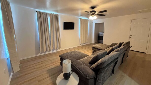 A living room with a sofa set, a ceiling fan, a TV, and a door. - 1BR Sleep 4 S Amarillo Corp Stays Tech + Hospital (Amarillo)