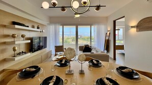 Ein modernes Esszimmer mit einem großen Esstisch für sechs Personen, einem Fernseher an der Wand und Blick auf die Stadtlandschaft durch große Fenster.