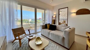 Ein modernes Wohnzimmer mit Sofa, Couchtisch und Sessel. Ein Balkon bietet Blick auf Gebäude und Grünflächen.