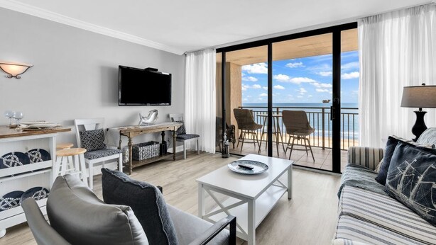 A modern living room with a flat-screen TV, a dining area, and a balcony with a view of the sea. - Ocean Forest Plaza 1006 (Myrtle Beach)