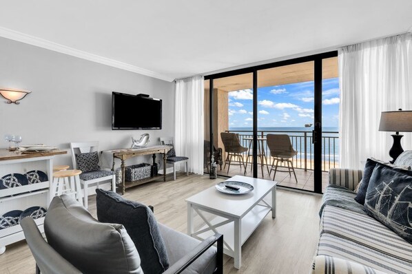 Ein modernes Wohnzimmer mit Flachbildfernseher, Essbereich und einem Balkon mit Meerblick.