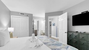 A hotel room with a bed, a dresser, a TV, and a door leading to another room. - Ocean Forest Plaza 1006 (Myrtle Beach)