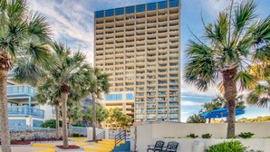 A high-rise hotel with multiple balconies, palm trees, and a clear sky. - Ocean Forest Plaza 1006 (Myrtle Beach)