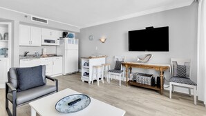 A modern living room with a dining area, kitchen, and a flat-screen TV mounted on the wall. - Ocean Forest Plaza 1006 (Myrtle Beach)