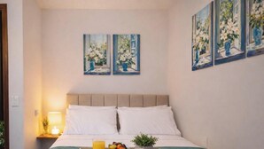 A hotel room with a bed, bedside table, lamp, fruit bowl, and three paintings on the wall. - Estúdio Floripa Norte - Florianópolis-SC (Florianópolis)