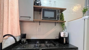 A compact kitchen with a microwave, toaster, and coffee maker on the countertop, a sink, and cabinets above the counter. - Estúdio Floripa Norte - Florianópolis-SC (Florianópolis)