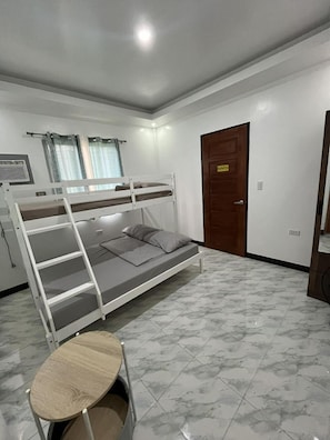 A bunk bed with a desk, a door, and a window with curtains.