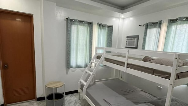 Quarto com cama beliche, mesa redonda pequena, porta e janela com cortinas.
