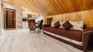 Un ambiente acogedor con techo de madera, un sofá con cojines estampados, una mesa de comedor y una zona de cocina.