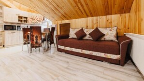 Una habitación acogedora con techo de madera, un sofá con cojines florales, una mesa de comedor con sillas y una zona de cocina.