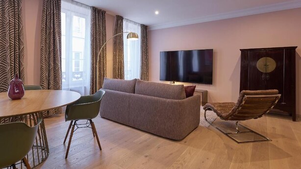 A modern living room with a sofa, a TV, a wooden cabinet, and a dining area with chairs.