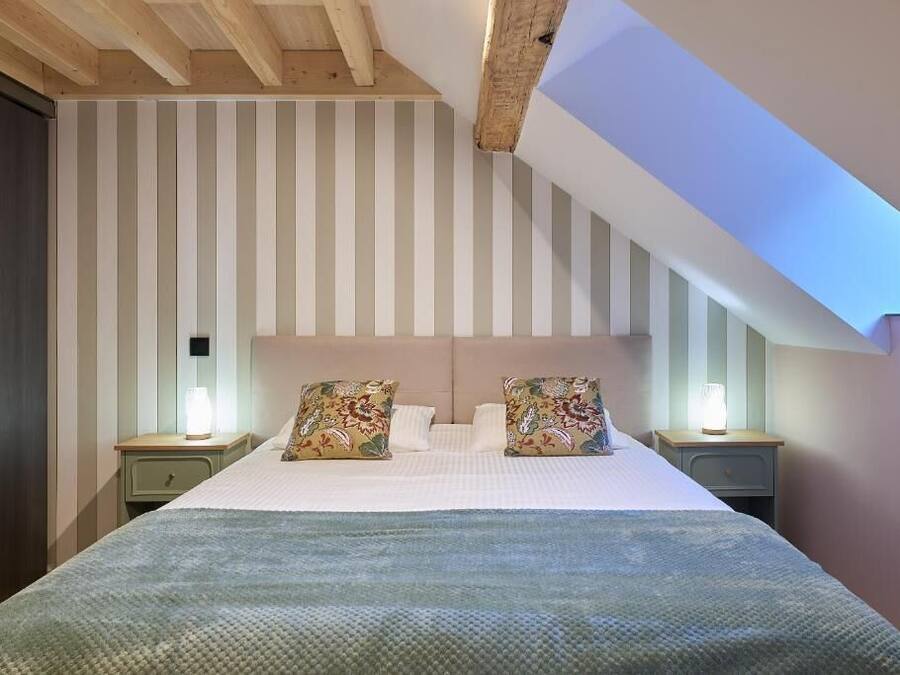 A bedroom with a sloped ceiling, a bed with patterned pillows, and bedside lamps.