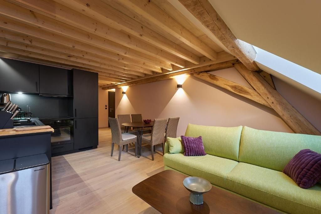 A modern loft with exposed wooden beams, a dining area, and a green sofa.
