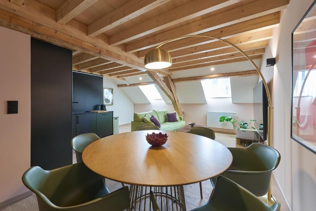 Een eetruimte met een ronde houten tafel, groene stoelen en een moderne hanglamp.