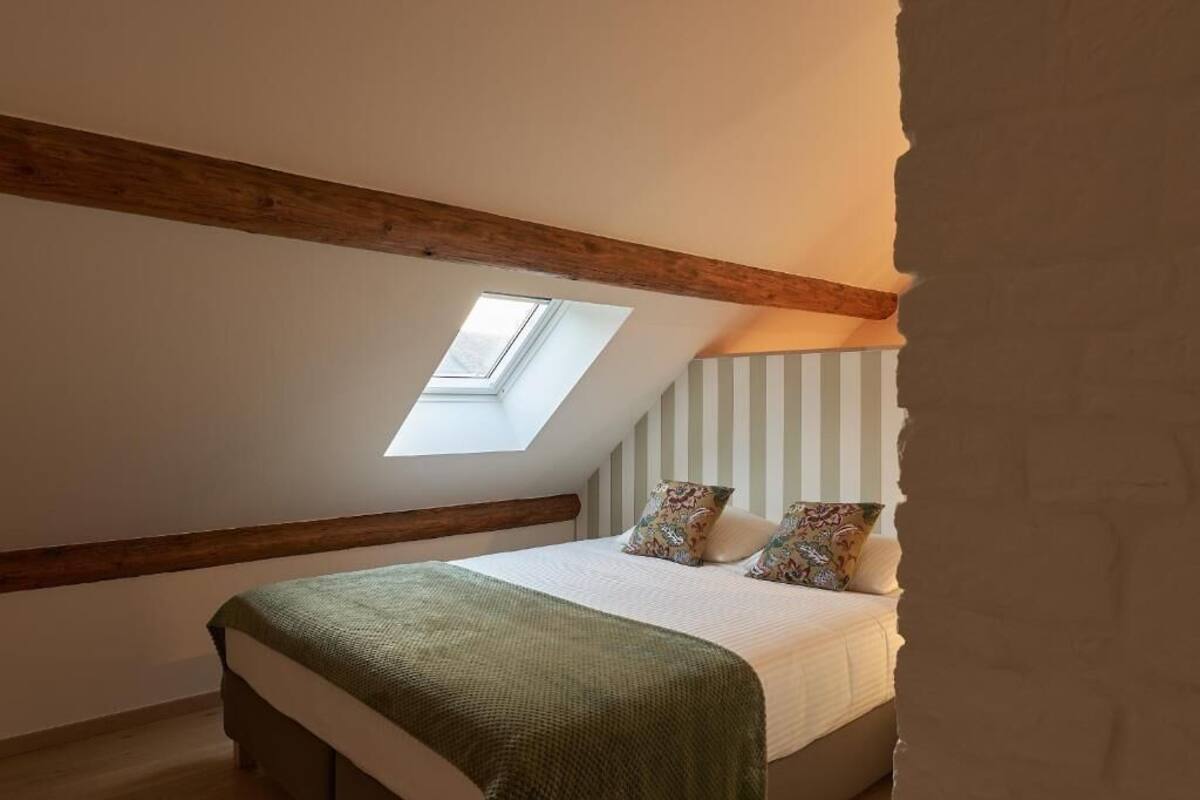 Una camera da letto con soffitto spiovente, una finestra a lucernario, un letto con coperta verde e carta da parati a righe.