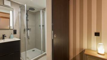 Un bagno moderno con cabina doccia in vetro, un mobile vanitario in legno e una lampada da comodino illuminata.