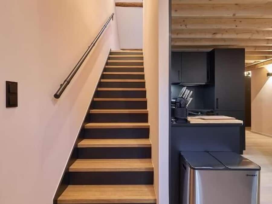 Una escalera moderna que lleva a una zona de cocina con refrigerador empotrado.