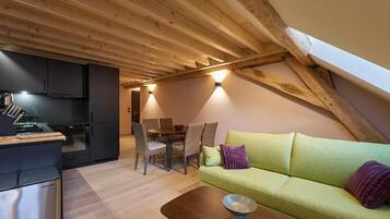 En moderne loftrum med synlige træbjælker, et spiseområde og en grøn sofa.