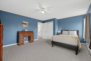 Ein Schlafzimmer mit Bett, Kommode, Deckenventilator und einer Tür zu einem anderen Raum.