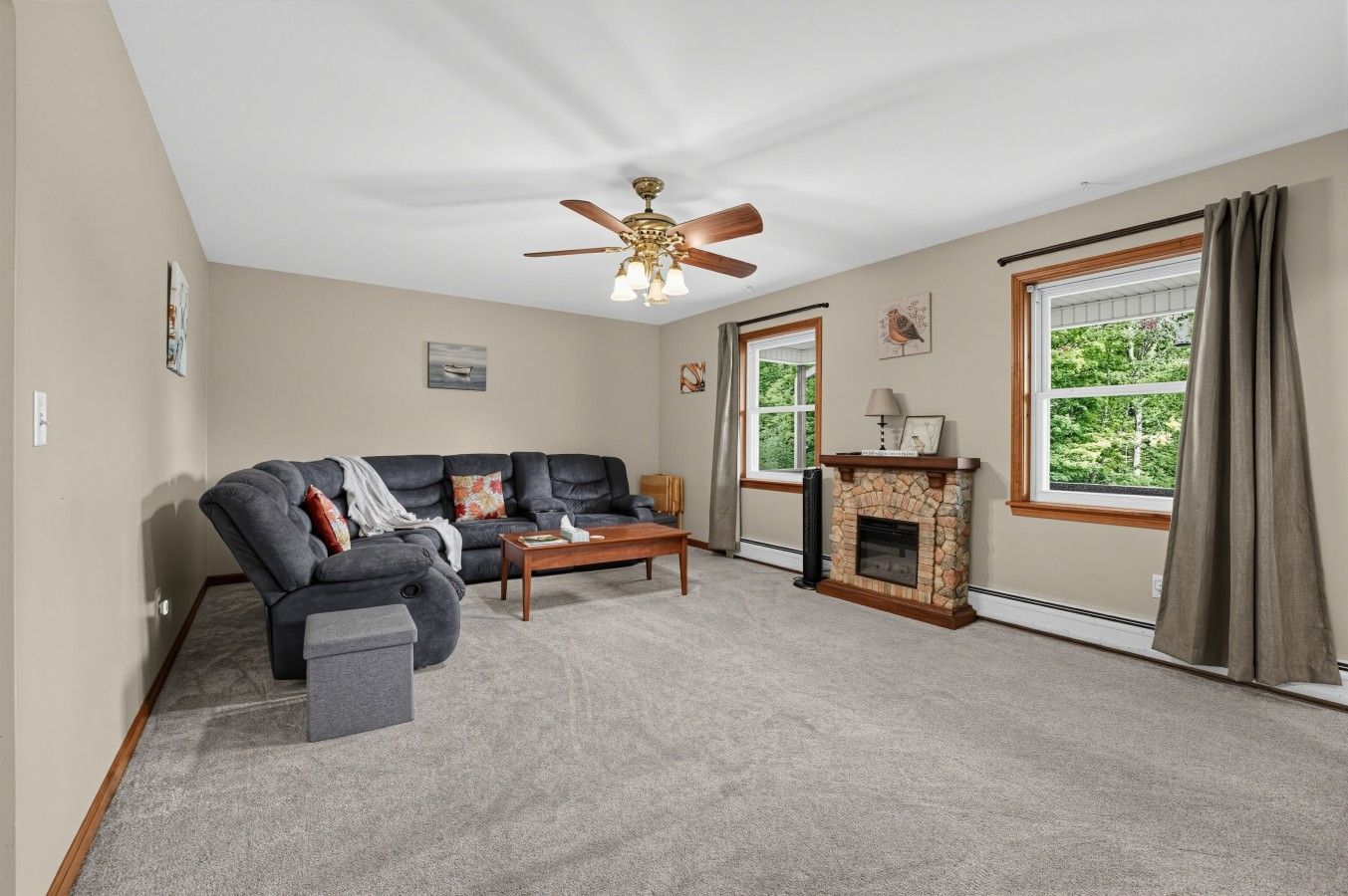 A living room with a sectional sofa, a fireplace, a ceiling fan, and large windows.