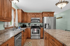A kitchen with wooden cabinets, stainless steel appliances, granite countertops, and a chandelier. - Vermont Mountain Retreat Near Lake Willoughby (Charleston)