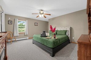 Une chambre à coucher comprenant un lit, un bureau, une chaise, un ventilateur de plafond et une fenêtre avec des rideaux.