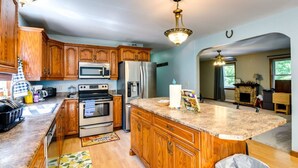 A kitchen with wooden cabinets, stainless steel appliances, a marble countertop, and a chandelier.