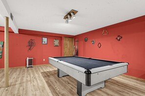 A pool table in a room with red walls, a wooden floor, and a ceiling light fixture. - Vermont Mountain Retreat Near Lake Willoughby (Charleston)