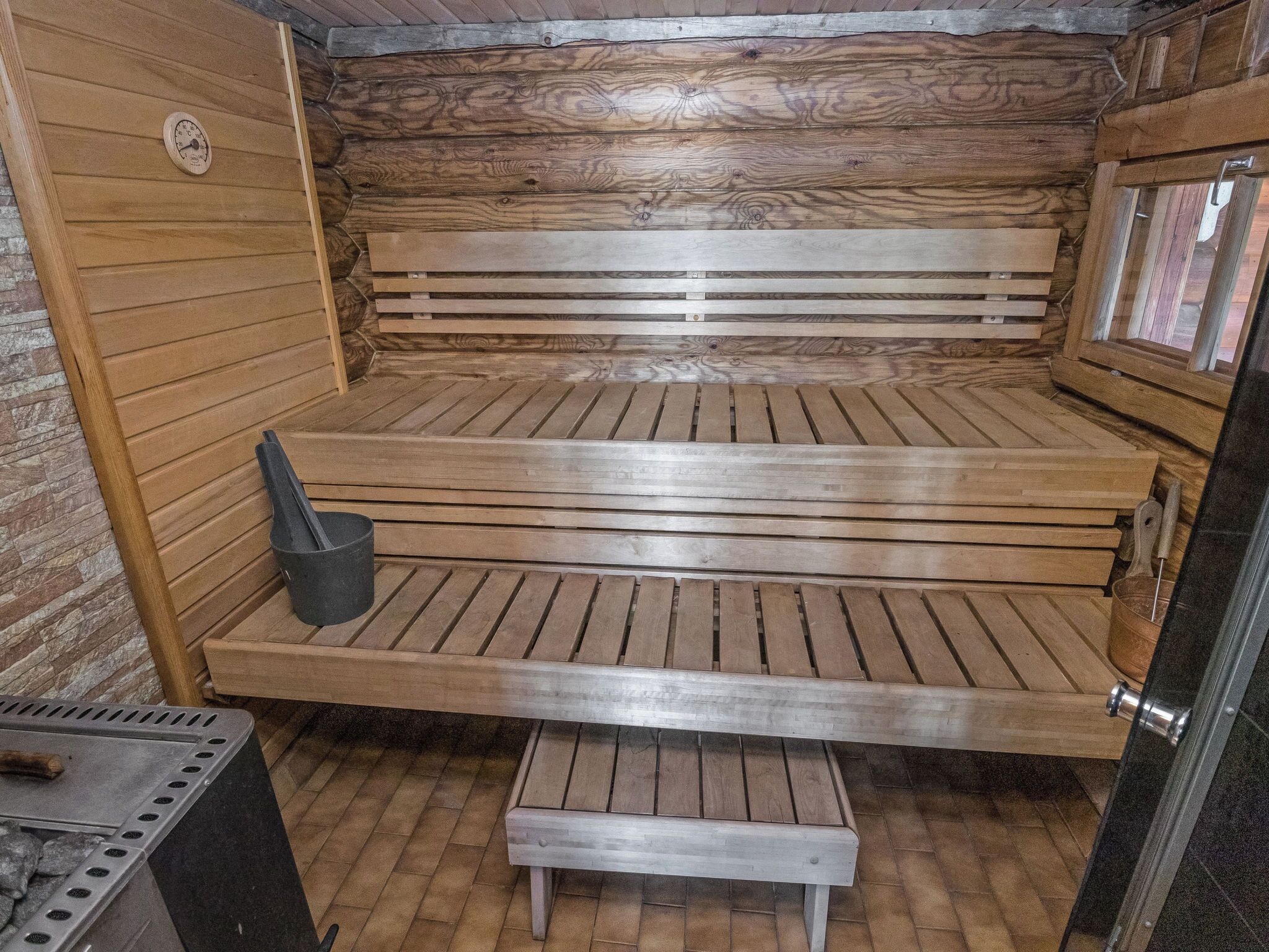 A sauna with wooden benches, a bench heater, and a bucket.