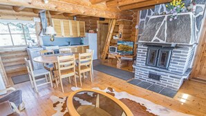 Interior de una cabaña con zona de comedor de madera, chimenea y alfombra de piel de vaca.