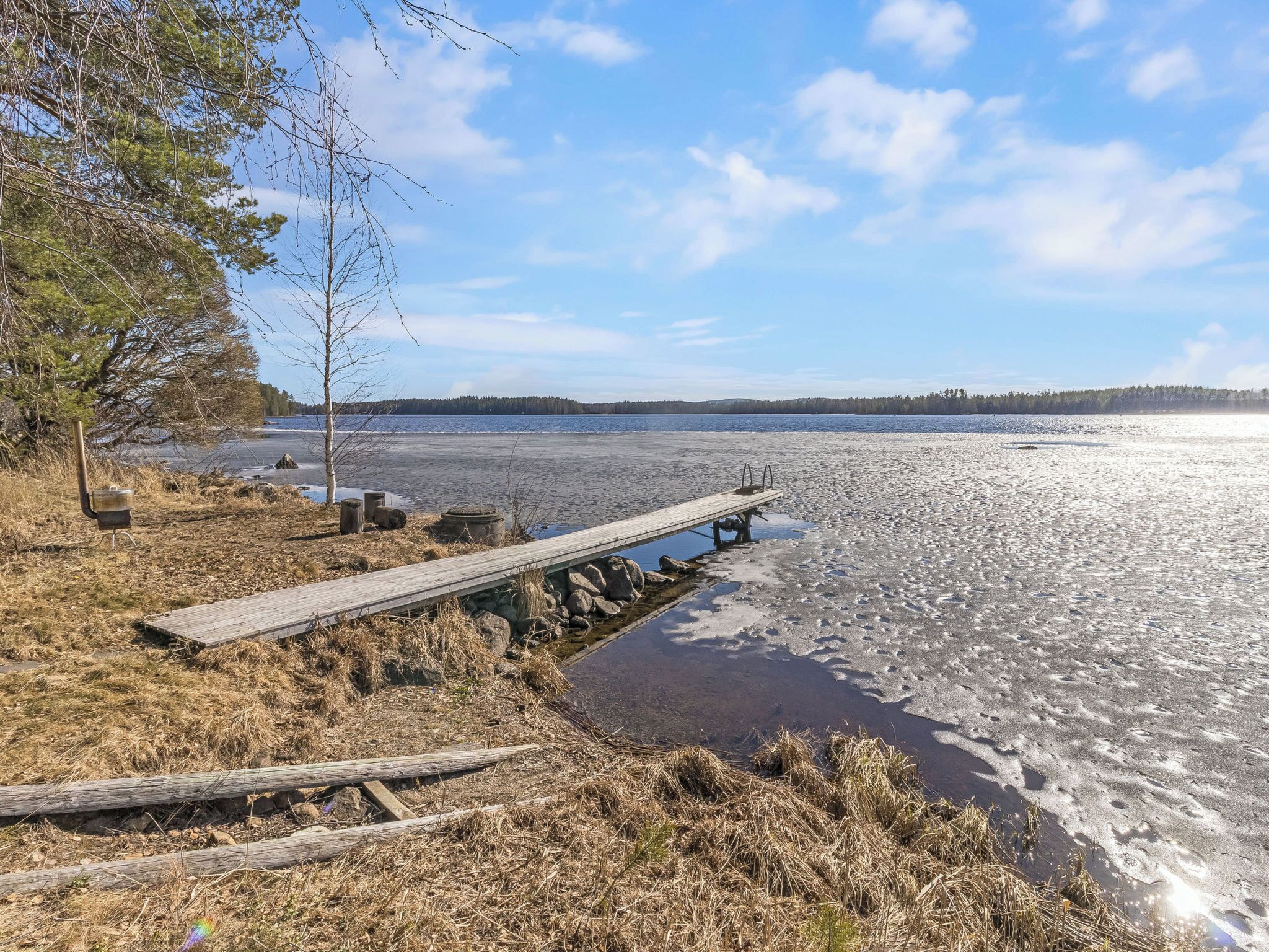 Une jetée en bois s’étendant dans un lac paisible, entourée d’herbes sèches et de quelques arbres.