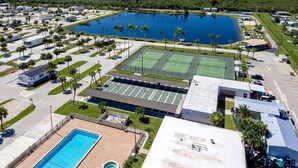 An aerial view of a campground with RVs, a tennis court, a pool, and a large lake. - BETTER THAN NEW - FULLY REMODELED - SHORT-TERM RENTAL FRIENDLY (Fort Myers)