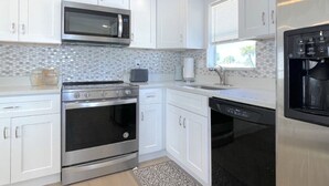 A modern kitchen with white cabinets, stainless steel appliances, a microwave, oven, dishwasher, and a refrigerator. - BETTER THAN NEW - FULLY REMODELED - SHORT-TERM RENTAL FRIENDLY (Fort Myers)