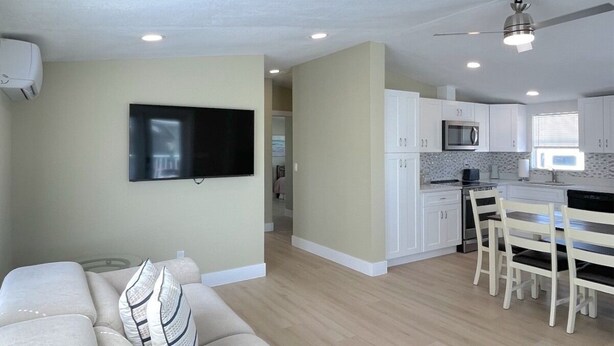 A modern living room with a sofa, a flat-screen TV, and a dining area with a table and chairs. - BETTER THAN NEW - FULLY REMODELED - SHORT-TERM RENTAL FRIENDLY (Fort Myers)