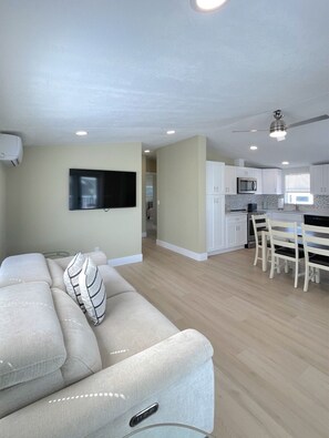 A modern living room with a sofa, a flat-screen TV, and a dining area with a table and chairs. - BETTER THAN NEW - FULLY REMODELED - SHORT-TERM RENTAL FRIENDLY (Fort Myers)
