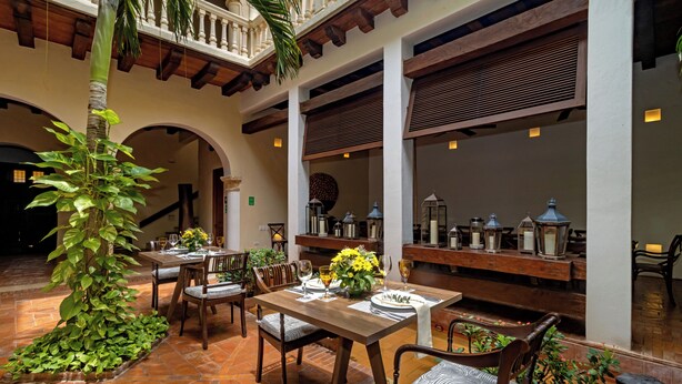 An outdoor patio with a dining table set for two, surrounded by chairs, a palm tree, and potted plants. - Luxury Old City with Pool and Jacuzzi, 8 Bedrooms (Cartagena de Indias)