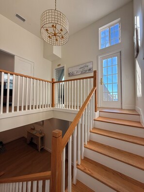 A staircase with wooden steps and white railings, a chandelier, and a door with windows. - Lux Oceanfront 4-Bed, 3-Bath Beach House. Sleeps 10. Buccaneer Beach, Oceanside (Oceanside)