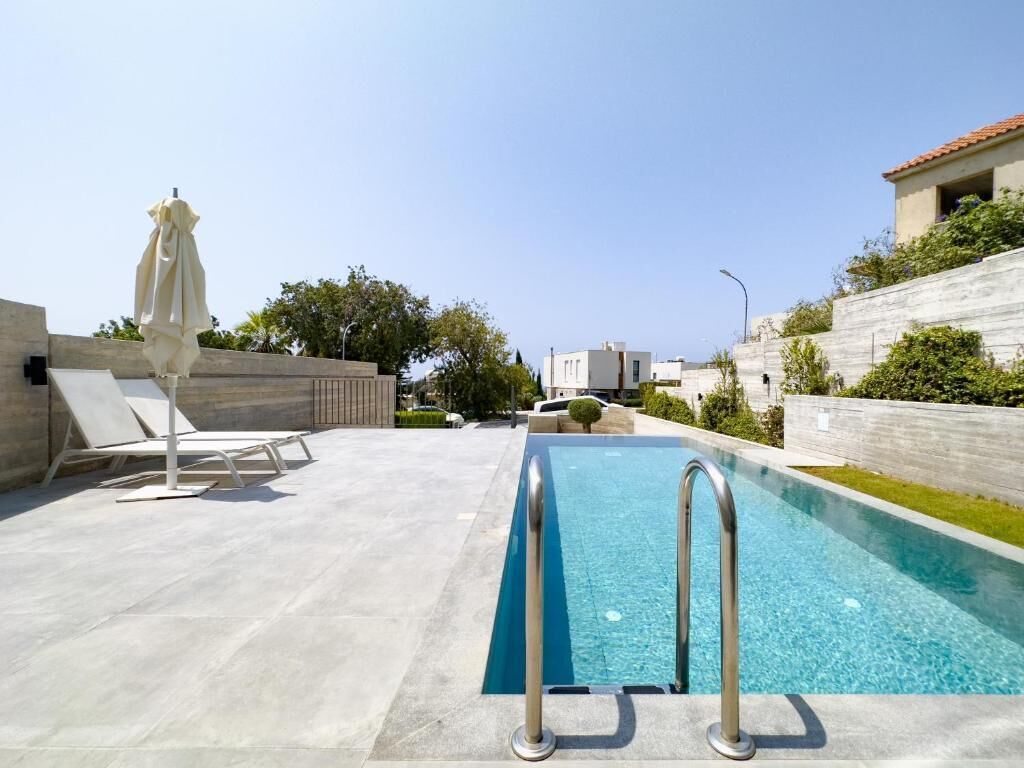 Piscina con escalera metálica, sillas de descanso y una sombrilla.