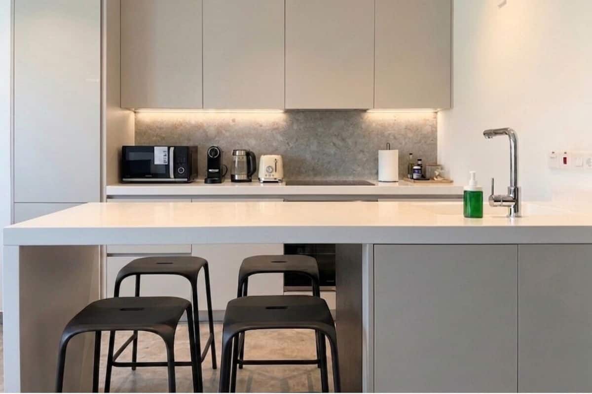 A modern kitchen with a white countertop, built-in appliances, and a bar area with stools.